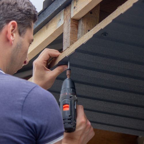 a man repairs the roof, tightens the self-tapping screw with a screwdriver. Selective focus