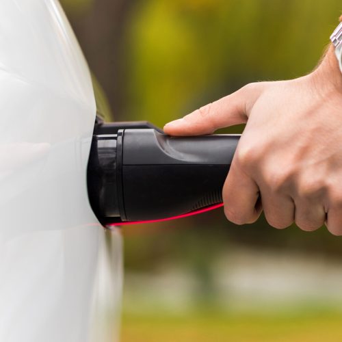 Close view of a man plugging charger into an electric car charging port